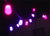 string light hanging outdoors at night, softly glowing pink and purple against a dark background